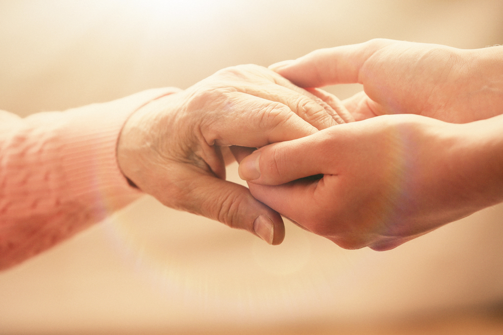 A senior woman and her adult daughter holding hands