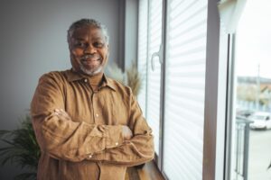 A smiling senior man poses near a window