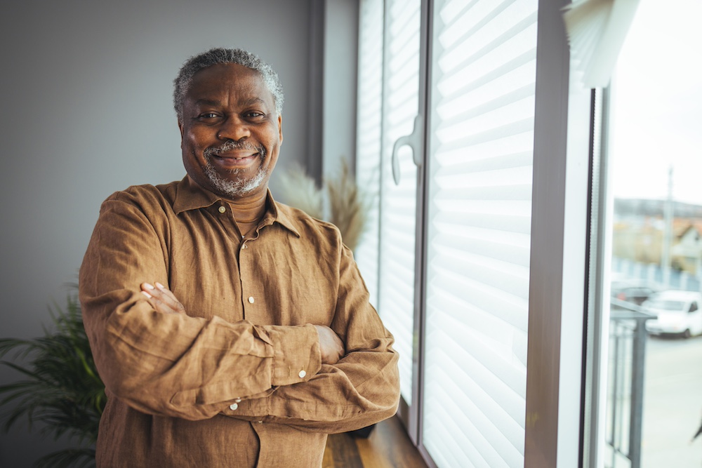 A smiling senior man poses near a window